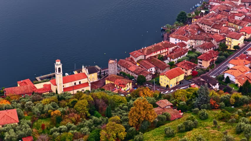 Aerial view of Lake Iseo with its historic lakeside village, church bell tower, and surrounding olive groves in Lombardy, Italy.