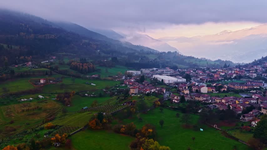 Aerial view of Lake Iseo and the surrounding town with rolling green hills, traditional rooftops, and distant mountains in Lombardy, Italy.