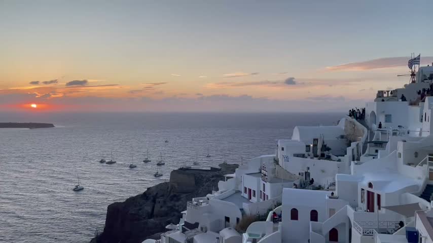 Sunset over the Aegean Sea viewed from Oia on Santorini, Greece, with a gradual zoom toward the setting sun. Scenic island footage featuring the sea horizon, evening light and caldera coastline.