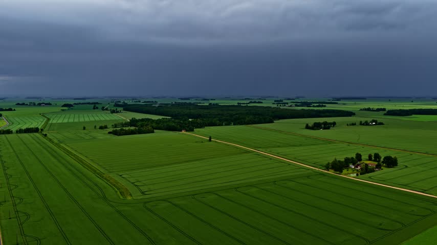 Aerial view of green fields and rural landscape under a dark stormy sky in Latvia.