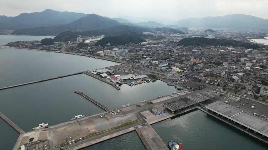Aerial view of Senzaki harbor with breakwaters and a coastal town backed by mountains in Nagato Japan.