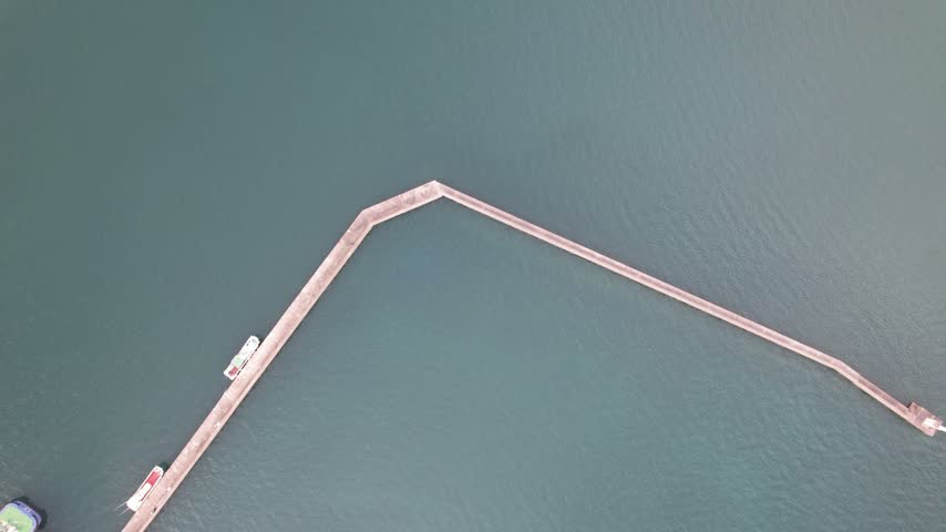 Overhead aerial view across harbor water and breakwaters toward quays and a road bridge in Senzaki Nagato Japan.