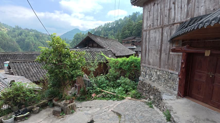 Wooden houses and a stone path with green hills at Langde Miao Village, Guizhou, China.