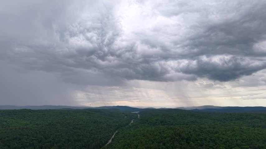 Wide aerial of rain clouds over road through green forest in Quebec, Canada