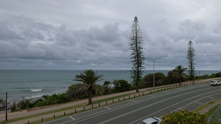 Slow-motion pan of a coastal road beside the ocean under overcast skies in Mooloolaba.