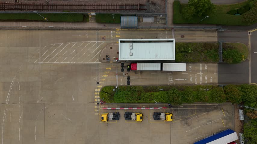 Aerial view of Daventry International Rail Freight Terminal with a truck at the security gate and parked yellow trucks in Kilsby, England, United Kingdom.