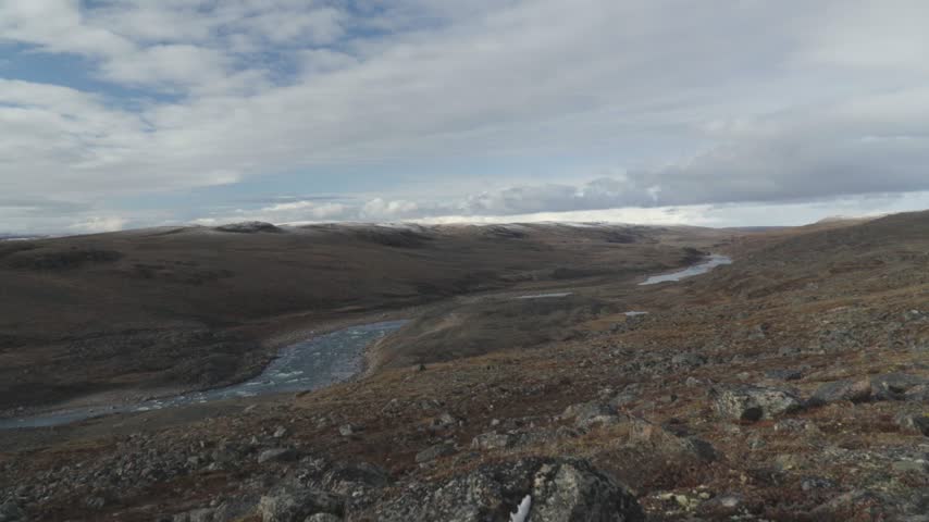 Wide camera shot panning right to left showcasing a winding river valley cutting through expansive subarctic tundra hills near Iqaluit