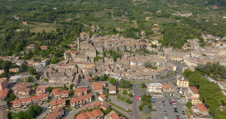 Panoramic aerial view of the town of Bolsena, in the province of Viterbo, Lazio, Italy, with the medieval old town, newer residential districts, a parking lot and wooded green hills around the town.