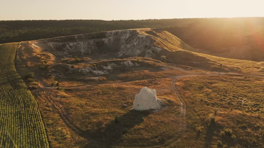 solitary white chalk mound in grassy farmland at golden sunset, aerial landscape view of ridge and r