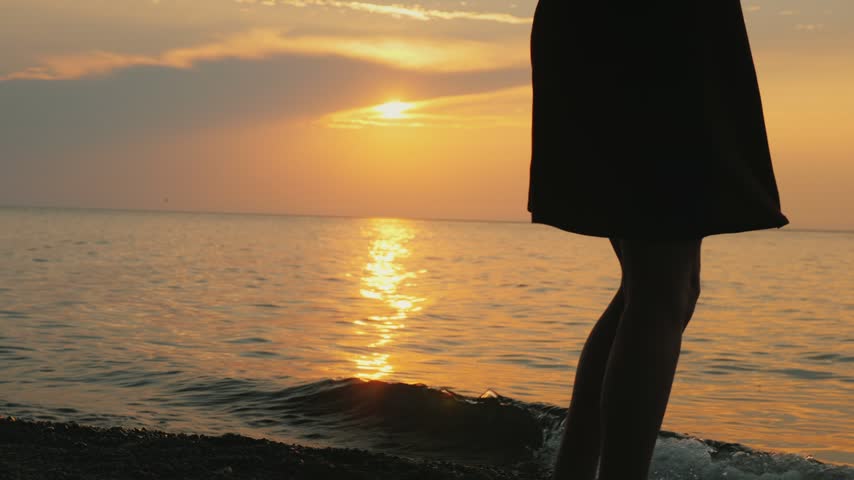Young woman silhouette dancing near ocean waves during golden hour summer evening cinematic footage.
