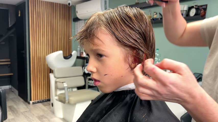 Little boy getting his hair trimmed by a professional hairdresser in a modern salon.