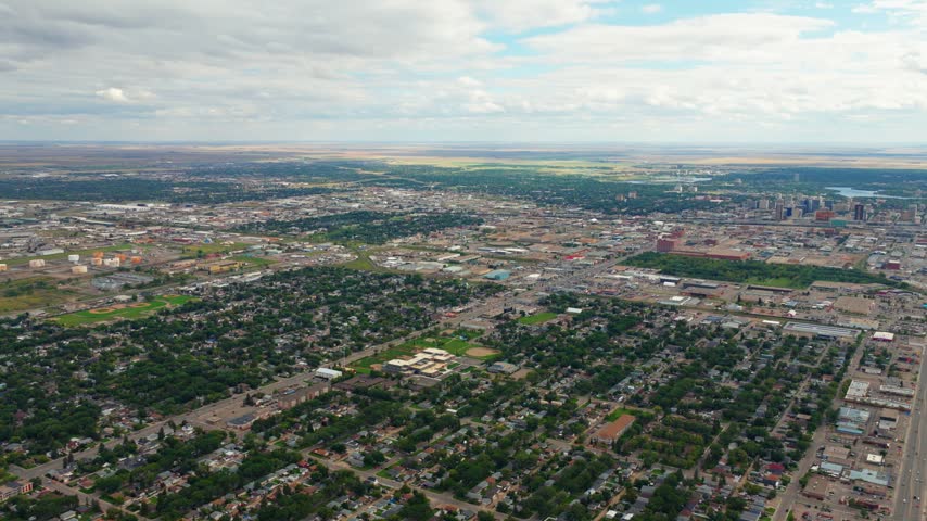 Drone shot angled downward over Regina, Saskatchewan, slowly panning right across neighborhoods and downtown under a blue summer sky with clouds.