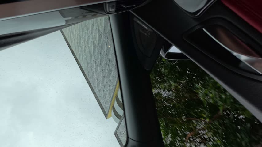 Upward view from inside a car driving past modern buildings under an overcast sky.