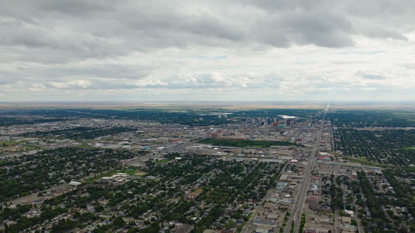 Slow moving aerial drone shot over Regina, Saskatchewan, showing the city, downtown skyline and long roadways beneath dramatic clouds on a summer day