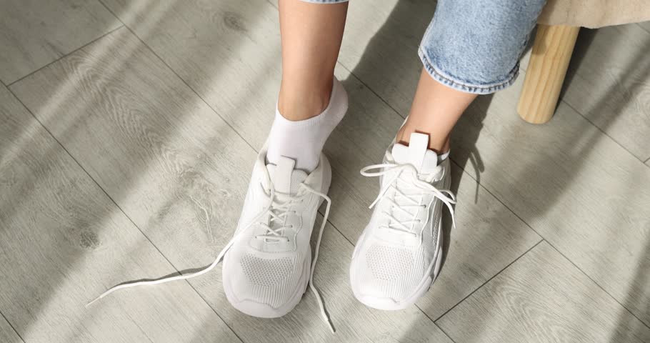 Woman putting on stylish sneaker indoors, above view