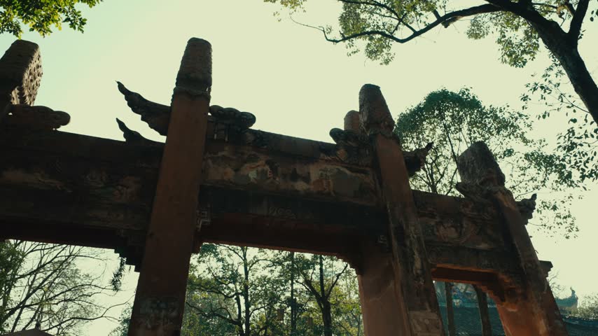 Weathered ceremonial gate framed by trees in Chongqing, China