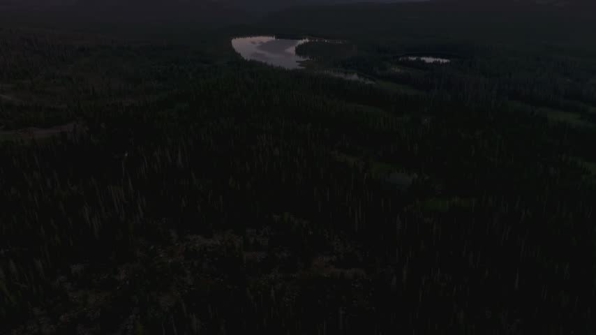 Aerial drone tilting up shot of a vibrant sunset over forested peaks and a valley of lakes, with Lost, Lily, Trial, and Teapot Lakes, on the Mirror Lake Scenic Byway in Uinta National Forest, Utah