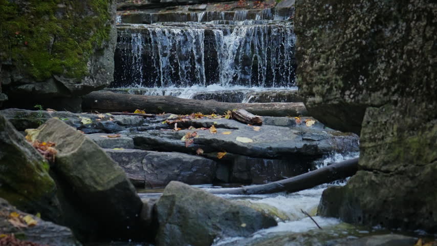 Streams of water plunge over stratified rock steps in Rockway Falls during autumn. Slow motion captures fine water spray hanging against dark rock walls.