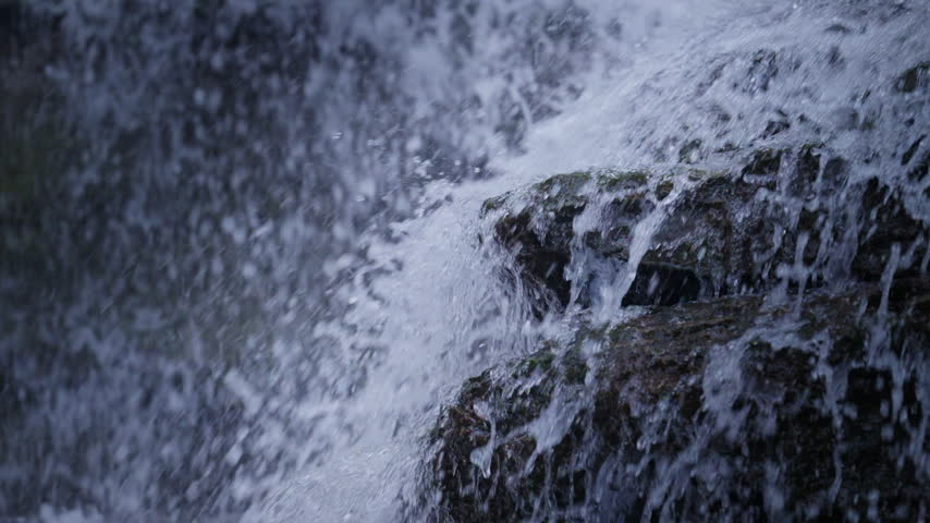 A forceful mountain stream plunges over a mossy rock edge at Rockway Falls, Ontario. The slow motion captures individual airborne droplets hanging momentarily before crashing downward.