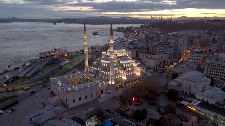 Aerial view of Istanbul at sunset, featuring the Bosphorus, a grand mosque, ferries, waterfront roads, historic buildings, and the city skyline glowing under a dramatic evening sky over Istanbul.