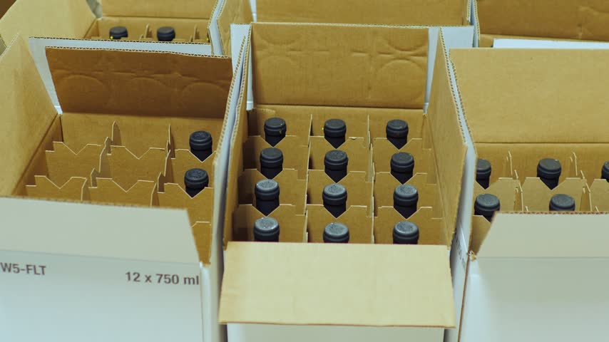 Worker hand packing bottles of red wine into carton boxes at winery bottling plant for distribution.