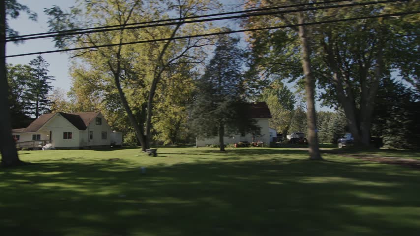 Traveling shot of quaint American residential houses along a tree lined suburban street in late summer or early fall afternoon.