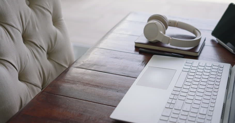 Slider is pushing camera right and forward showing laptop headset notes tablet glare to show desk. Device, notebooks, headphones, reflections, daylight, workspace, window