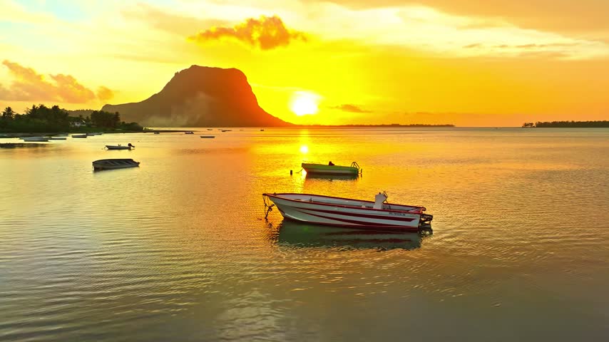 Aerial video of a boat floating on a calm lake during golden hour sunset, with a mountain silhouette in Switzerland.