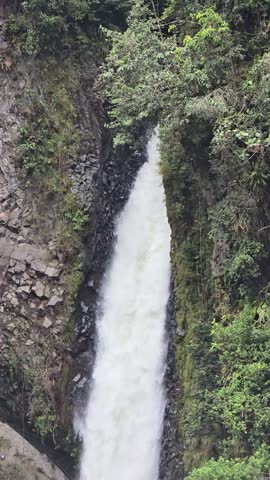 Tall narrow waterfall dropping through a steep green rocky gorge