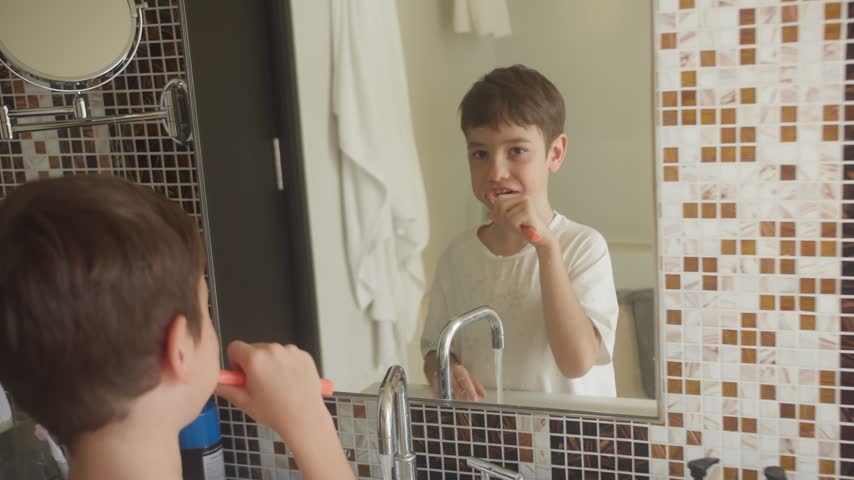 Young boy brushing his teeth with a toothbrush in a bright bathroom at home, practicing daily oral hygiene during his morning routine.