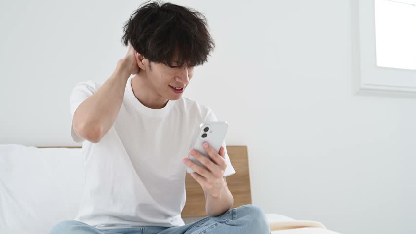 Japanese Man in His Thirties Looking Worried While Using a Smartphone