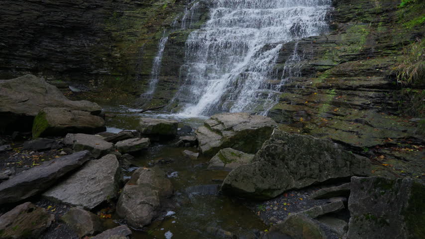 Cold stream water rushes over low rock steps and splashes past large boulders at Rockway Falls, Ontario. The layered stone wall rises behind the clear autumn riverbed.