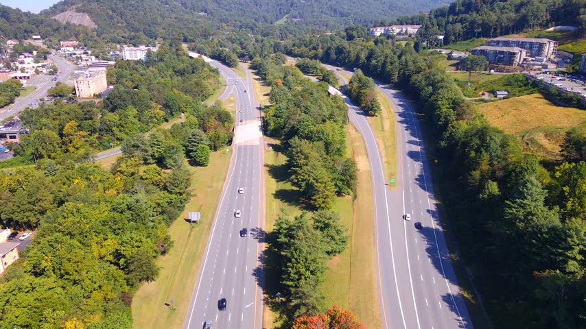 Traffic follows a divided highway between wooded hills and Asheville buildings.