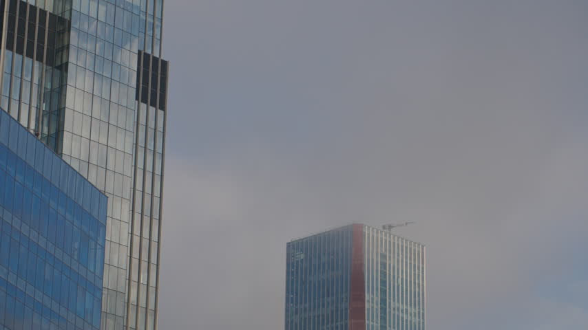 A moving view frames modern office towers with blue reflective windows and geometric facades beneath a gray sky.