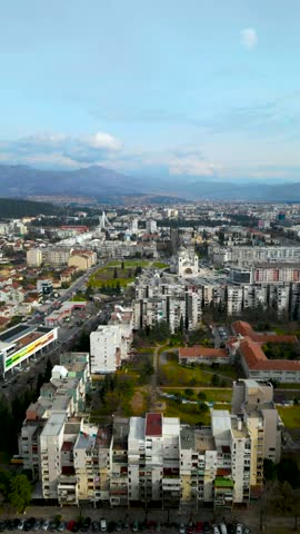Vertical aerial view of Podgorica cityscape with Cathedral of the Resurrection of Christ and mountains in background, Montenegro