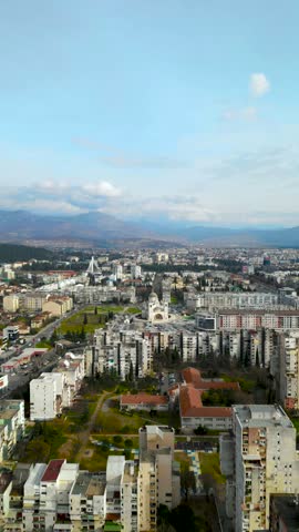 Vertical aerial view of residential buildings and Cathedral of the Resurrection of Christ in Podgorica with mountains in background, Montenegro