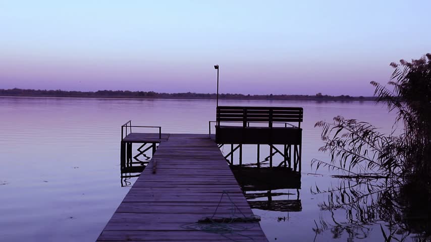 Pier extending into calm purple water during peaceful evening twilight after sunset