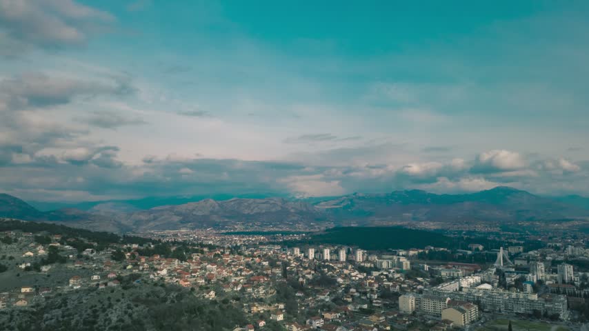 Timelapse high angle view of Podgorica city landscape with fast moving clouds and mountains in background, Montenegro