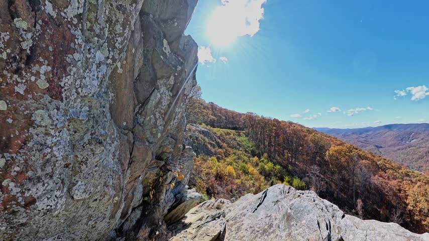 Textured stone ledges frame distant Virginia mountains above orange and green forest.
