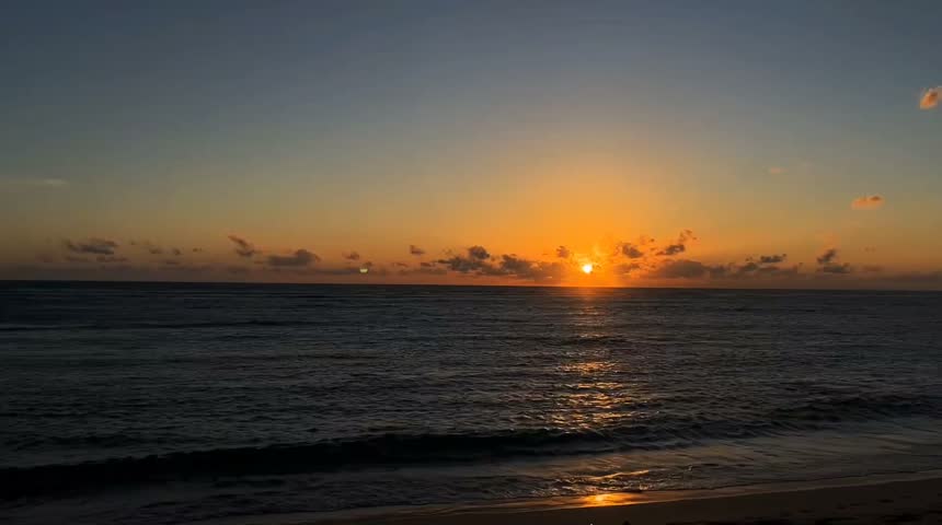 Beautiful orange sunset over the ocean, with golden sunlight reflecting on gentle waves and a sandy beach. Peaceful coastal scenery under a warm evening sky.
