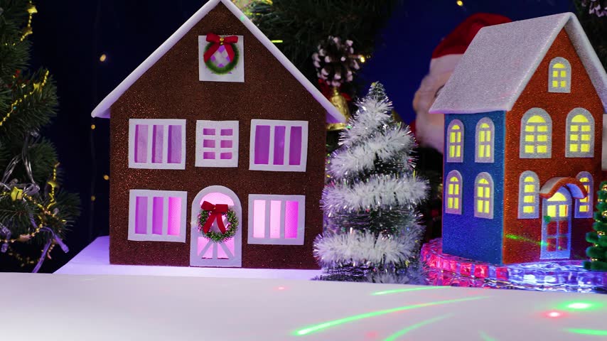A yellow car pulls up to an orange car, some little houses spinning on a base, and a snowman holding a Christmas lantern