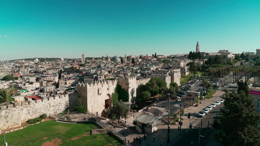 A wide afternoon view of Damascus gate at the old city of east Jerusalem, where Mosques and Churches, are intertwined with old houses, as filmed from a nearby rooftop. people are walking in and out.