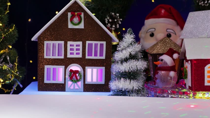 A yellow car pulls up to an orange car, some little houses spinning on a base, and a snowman holding a Christmas lantern