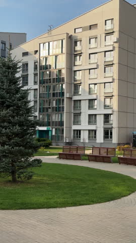 Courtyard of modern residential complex with lawn and paths. Benches in inner yard near multistory buildings. Vertical architecture of contemporary quarter.