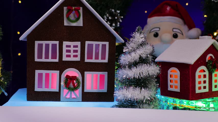 A yellow car pulls up to an orange car, some little houses spinning on a base, and a snowman holding a Christmas lantern