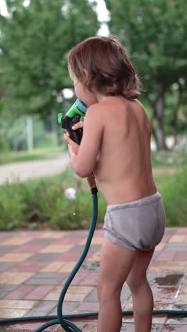 A small boy plays with a garden hose outside. The boy enjoys spraying water while standing on the patio.