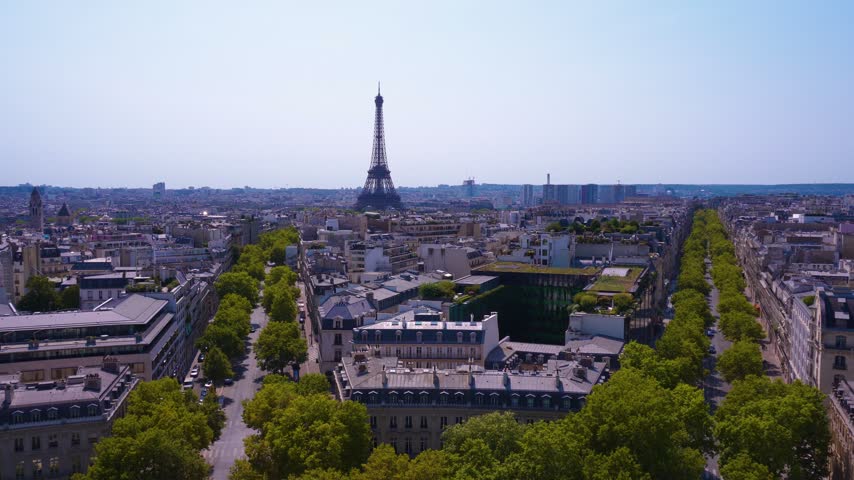 An aerial high-angle video of the Paris cityscape in France, featuring the iconic Eiffel Tower rising in the distance under a clear sky. The shot highlights typical Haussmann architecture, dense urban rooftops, and wide tree-lined boulevards with daylight illumination. Ideal for travel documentaries, tourism promos, and European cityscape backgrounds.