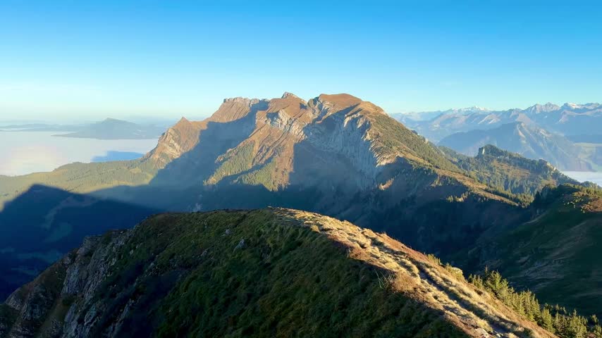 Panoramic view of the Pilatus mountain range from Mittaggüpfi, Switzerland, bathed in soft evening light beneath a deep blue sky, evoking freedom, inner peace and connection with nature.
