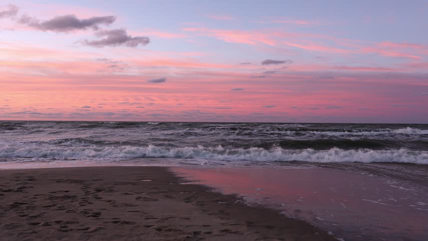 Pink sunset reflecting on wet sand as sea waves wash over beach