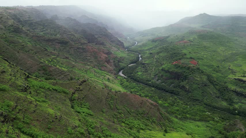 Aerial drone view of a foggy canyon with red soil patches and a winding river